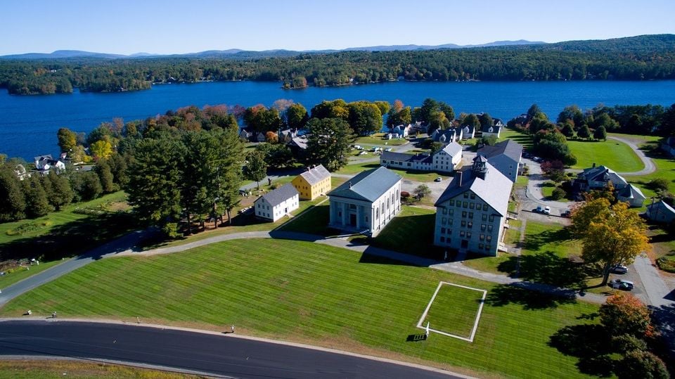Aerial view of lakeside buildings and broad lawns, with wooded hills across the water.