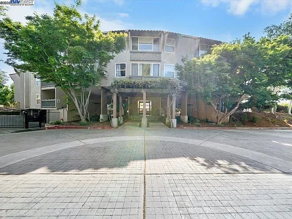 Apartment building with a covered central entrance, mature trees, and a broad paved courtyard.