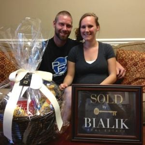 Michael and Jenifer celebrate their closing with a gift basket and Bialik Real Estate sold sign.