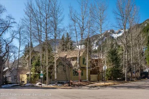 Tan multi-story home behind leafless trees, with snow-covered mountains in the background.