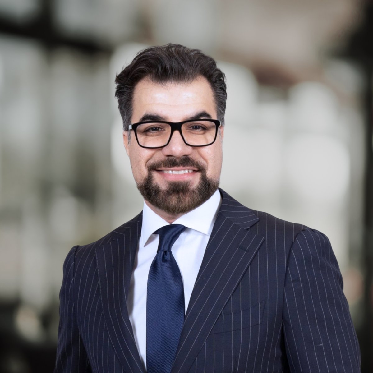 Farbod Yarahmadi smiling in glasses and a navy pinstripe suit.