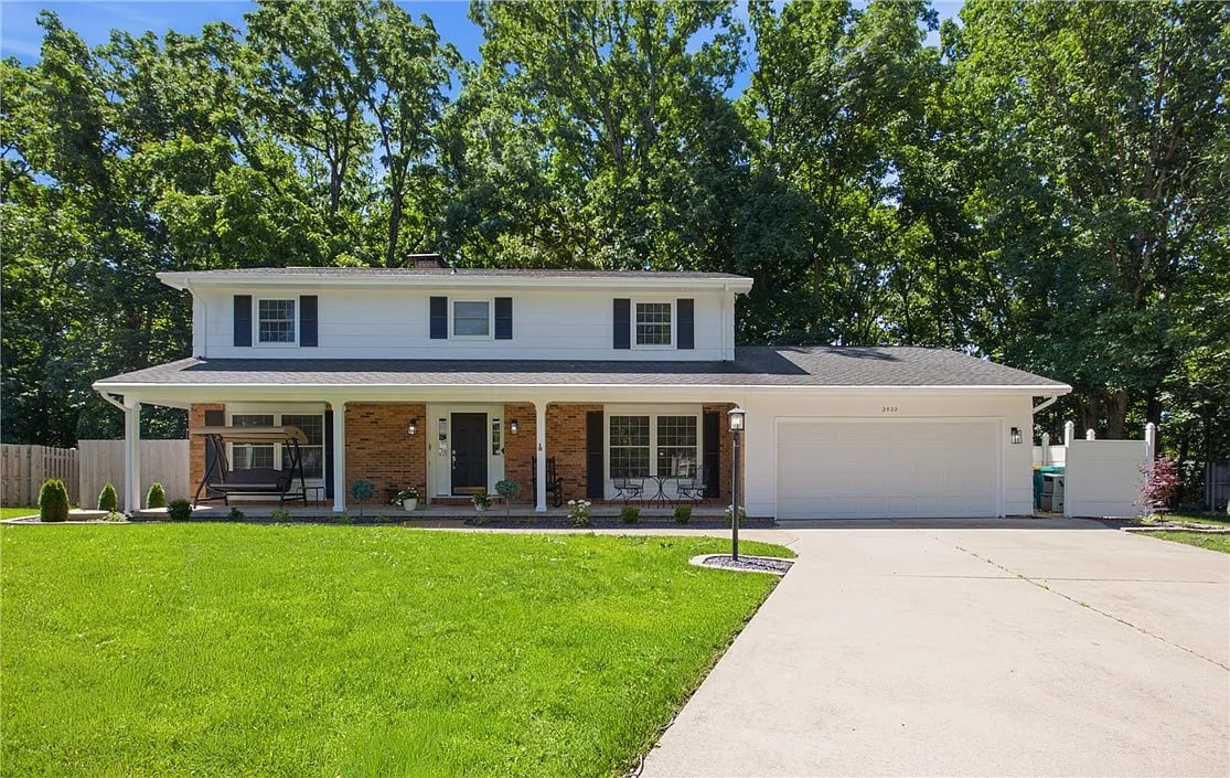 Two-story white-and-brick home with a covered porch, attached garage, and broad front lawn.