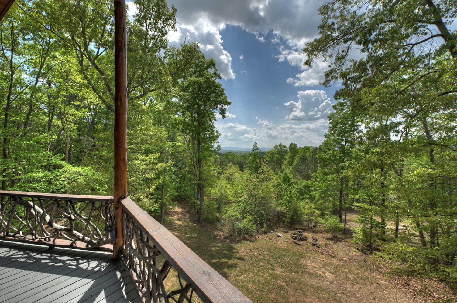 Wooden deck overlooking forest and distant mountain ridges beneath a partly cloudy sky.