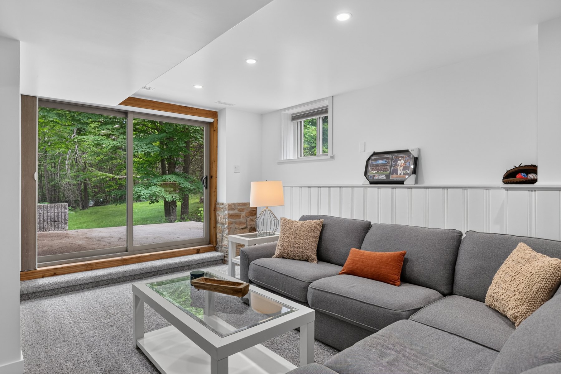 Living room with a gray sectional beside sliding glass doors overlooking a leafy yard.
