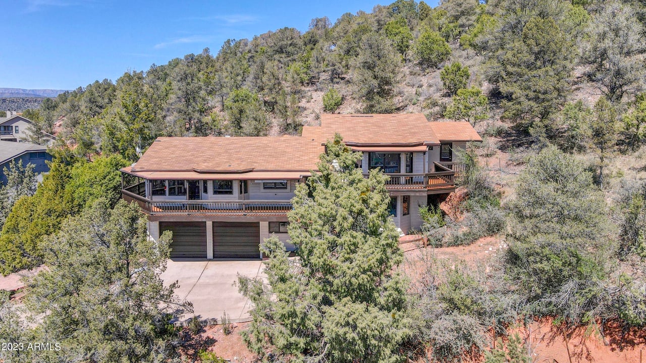 Hillside home with wraparound balconies and a two-car garage, surrounded by trees.