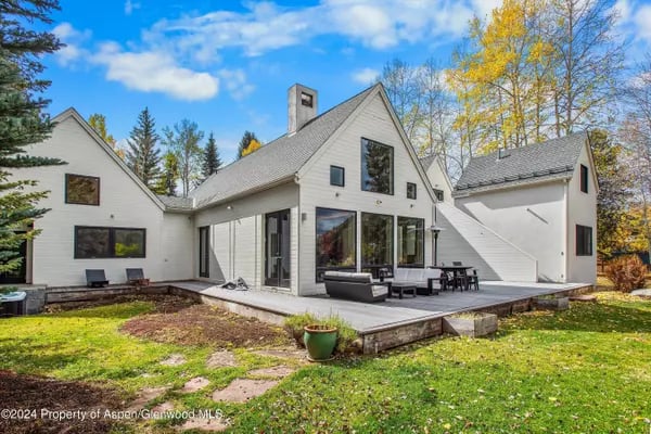 Modern white house with a broad patio, outdoor seating, and lawn.