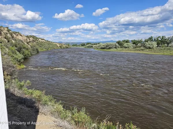 River flowing between green banks beneath a cloud-filled sky, with distant hills.
