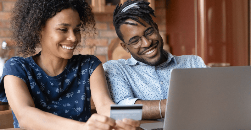 A couple review a laptop together as one holds a credit card.