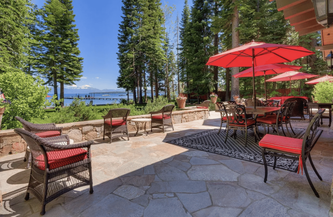 Lakefront patio with red umbrellas and dining furniture overlooking the water and distant mountains.
