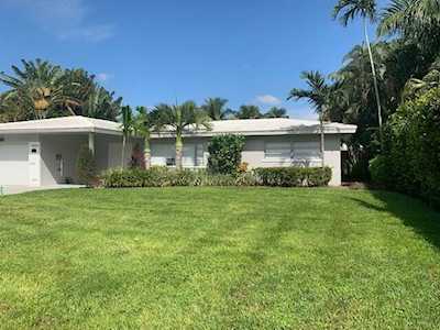 Single-story home with a broad green lawn, palm trees, and tropical landscaping.
