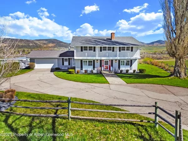 White two-story home with an attached garage, broad driveway, and mountain hills behind it.
