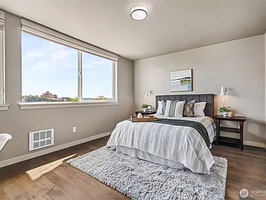 Bedroom with a king bed, gray bedding, large window, and hardwood floors.