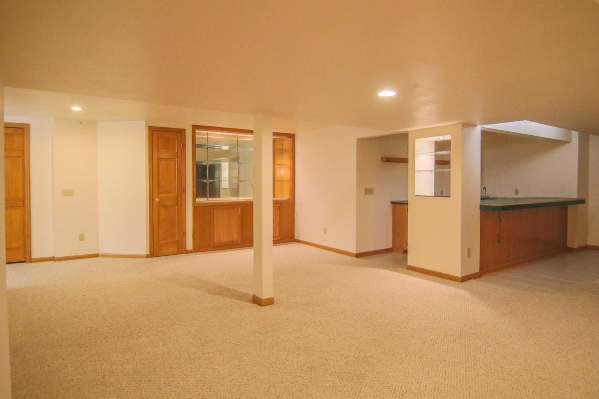 Vacant finished basement with beige carpet, wooden doors, and a built-in wet bar.