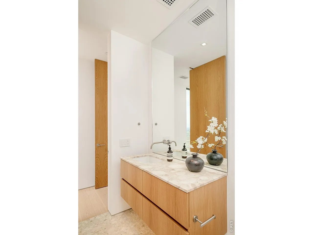 Modern bathroom vanity with pale stone countertop, light wood cabinets, and a large mirror.