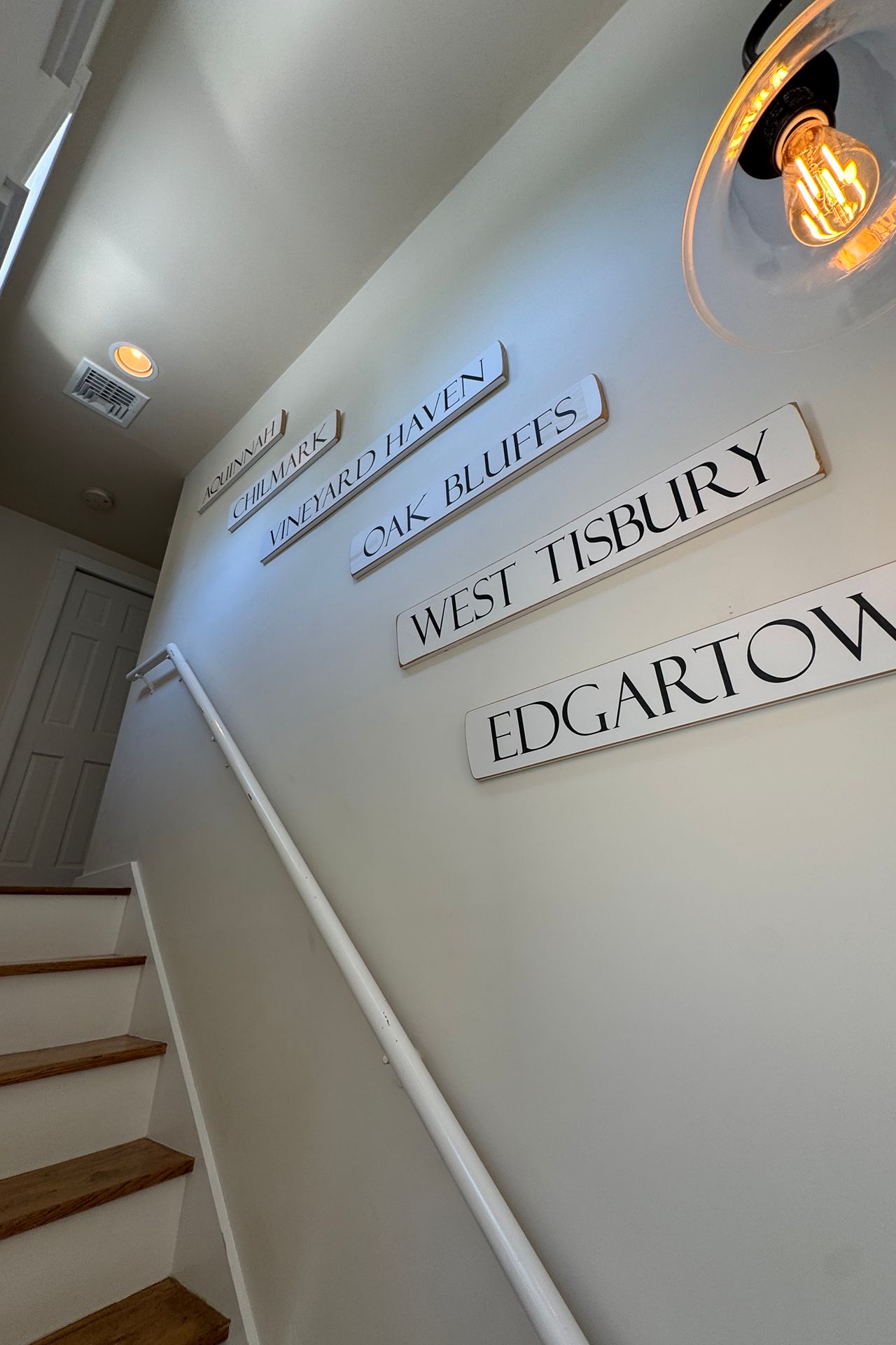Staircase with white walls, wood-tread steps, and signs naming Martha’s Vineyard towns.