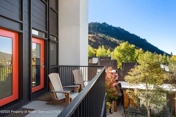 Balcony with wooden chairs overlooks leafy trees, neighboring homes, and a mountain slope.