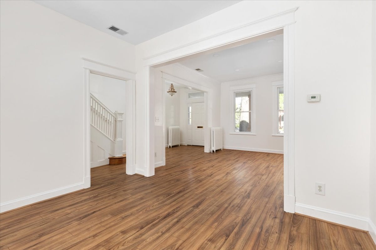 Empty living area with hardwood floors, a broad doorway, and a staircase to the left.