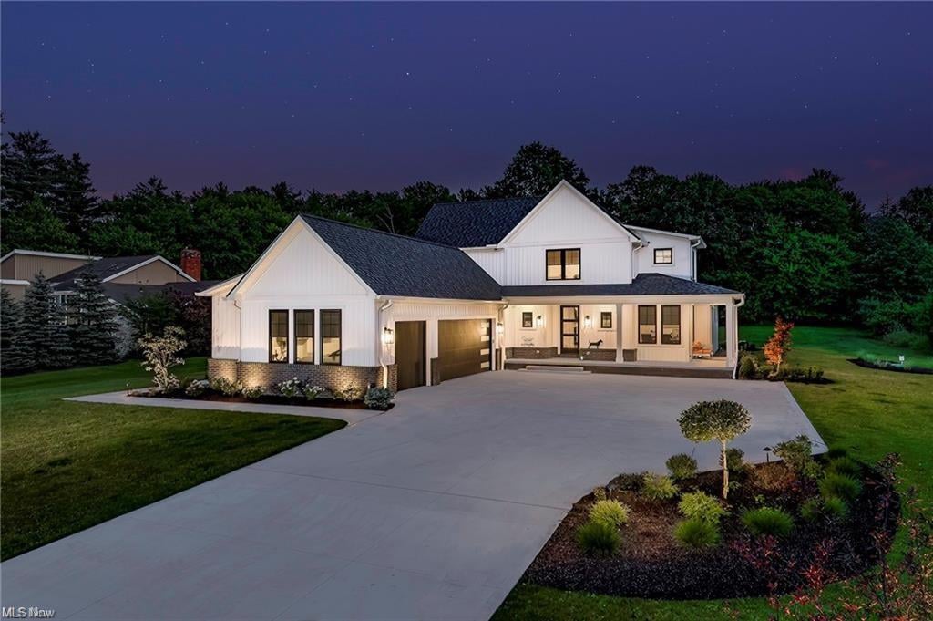 White two-story home at night, with a broad driveway, lit windows, and landscaped grounds.