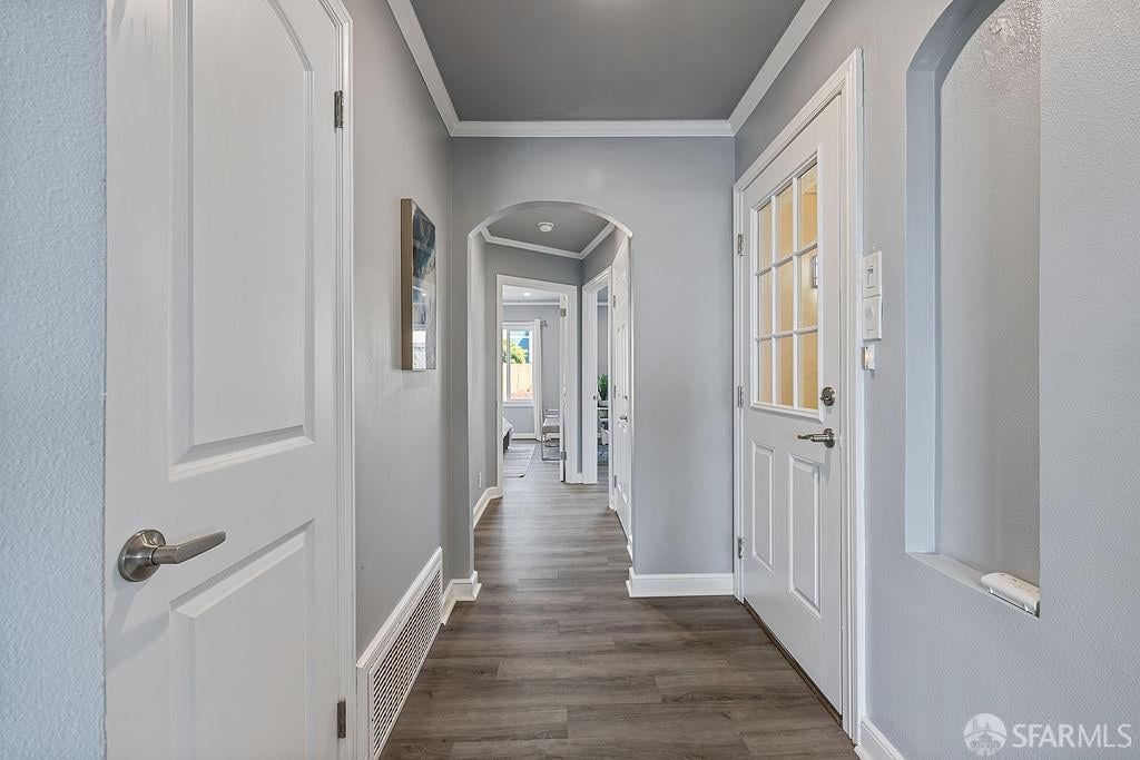 Interior hallway with dark plank flooring, white paneled doors, and an arched opening.