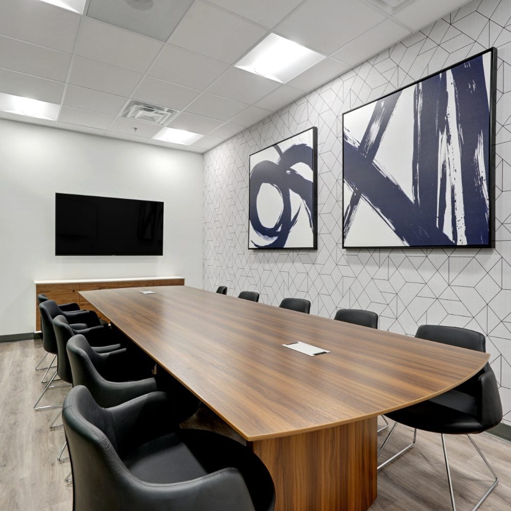 Conference room with a long wood table, black chairs, and abstract artwork on a geometric wall.