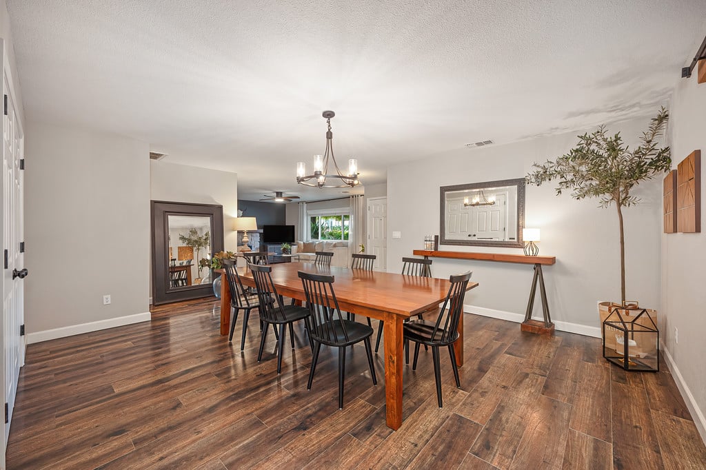 Dining room with a long wooden table, black chairs, and dark wood-look floors.