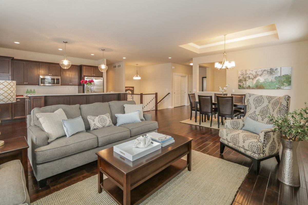 Open-plan living room with gray seating, dark wood floors, and kitchen and dining areas beyond.