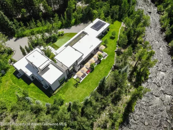 Modern flat-roof home with solar panels and lawn beside a rocky riverbed.