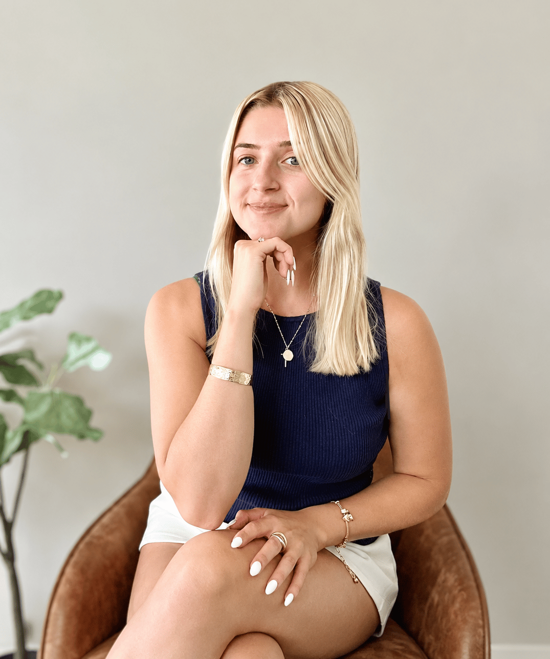 Anna Hebel seated in a brown chair, wearing a navy top and white shorts.