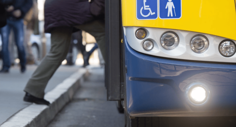 Pedestrian steps off a curb beside a city bus displaying wheelchair accessibility symbols.