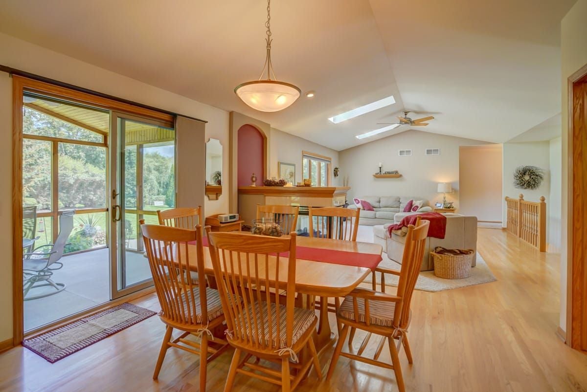 Dining and living room with a wood table, fireplace, vaulted ceiling, skylights, and patio doors.