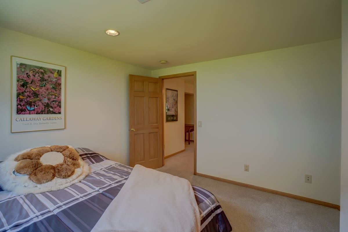 Furnished bedroom with plaid bedding, layered pillows, and an open wooden door.