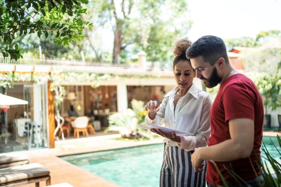 A woman and man review a checklist beside a swimming pool at a vacation rental.