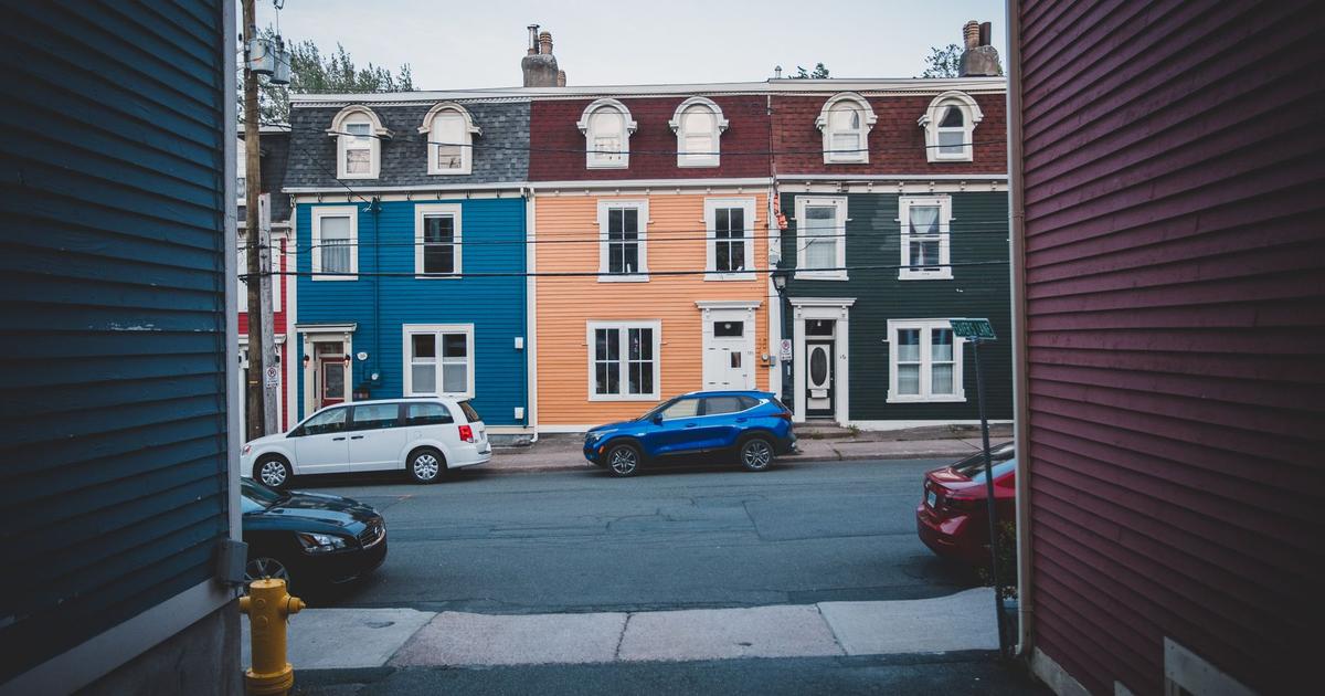 Row of attached townhouses with painted wood siding and mansard roofs along a residential street