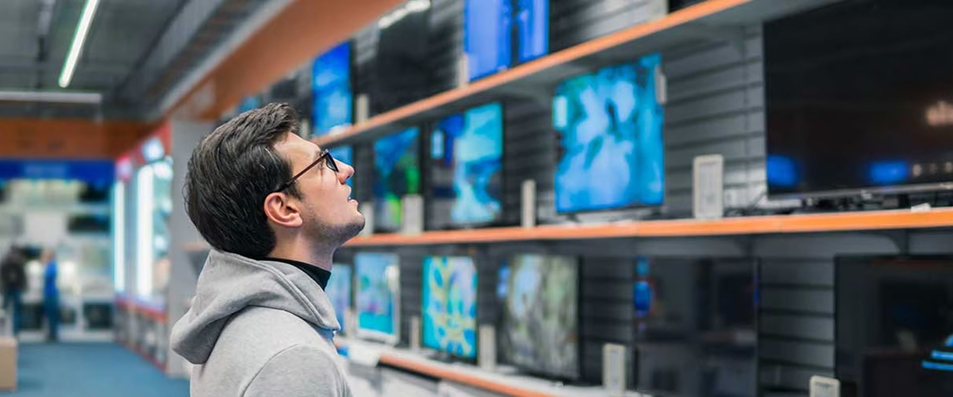 Man looks up at televisions in an electronics store.