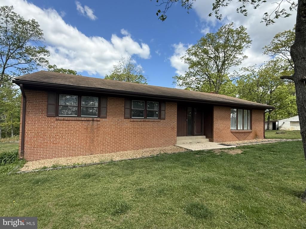 Single-story red brick house with dark shutters, recessed entrance, and a broad front lawn.