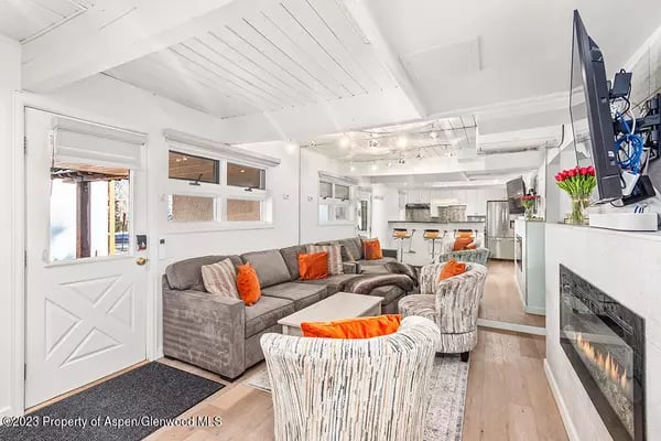 Open-plan living room with gray sofas, orange accents, a modern fireplace, and kitchen beyond.