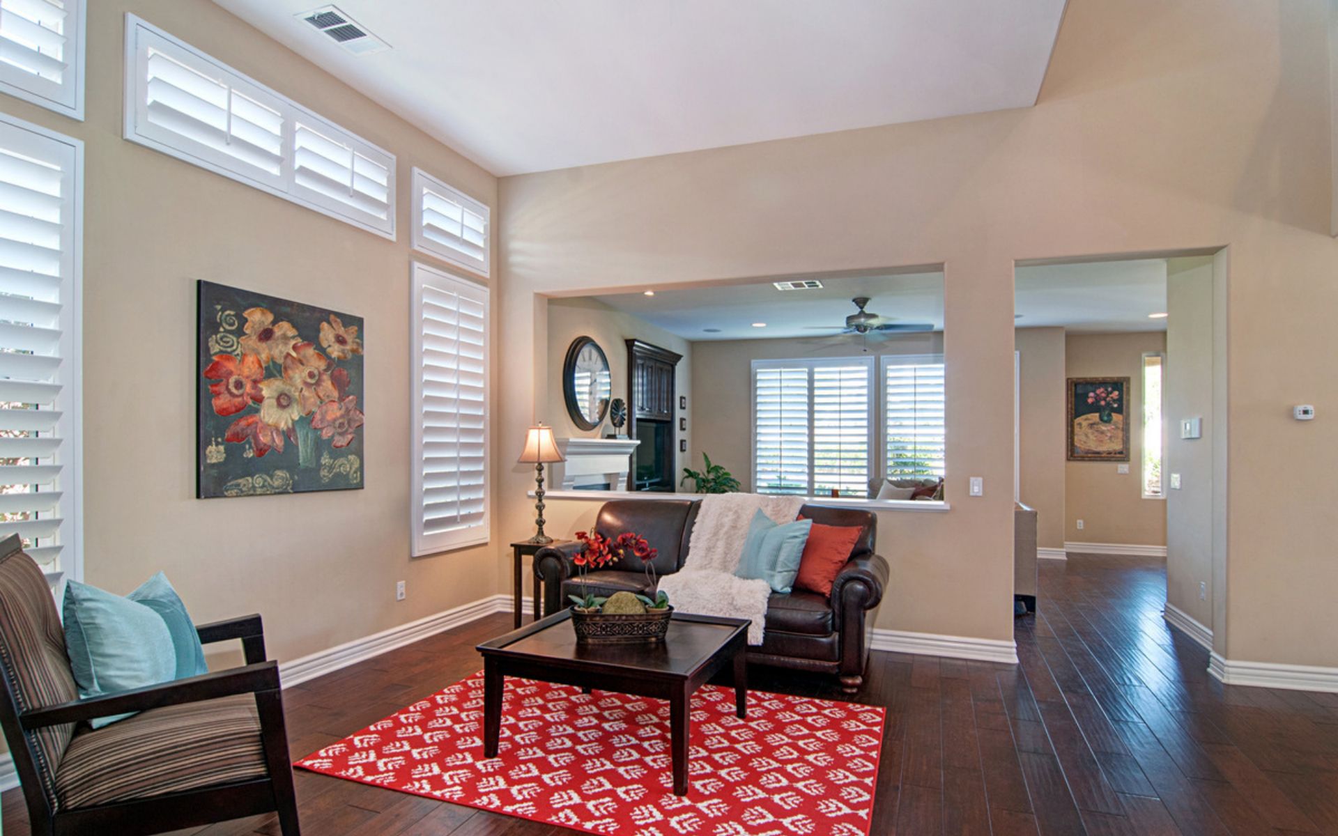 Furnished living room with plantation shutters, dark wood floors, and a red patterned rug.