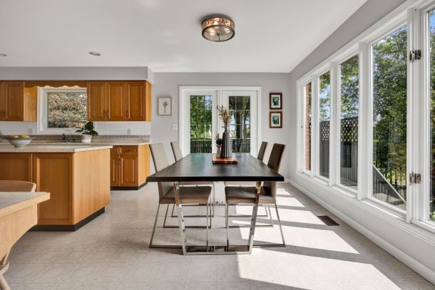 Dining area with a dark table beside a wood-cabinet kitchen and large windows.