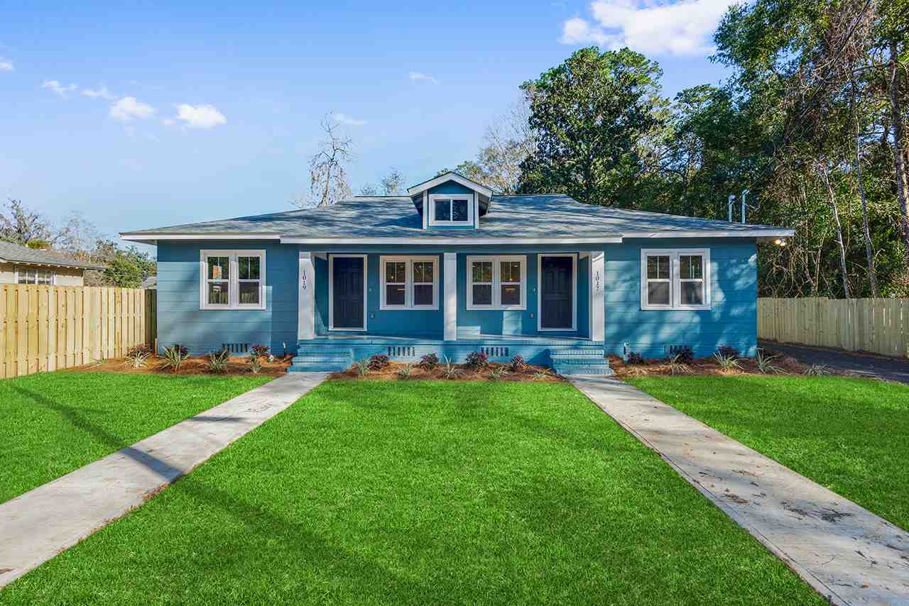 A blue house surrounded by a green lawn and a white fence, creating a picturesque suburban scene.