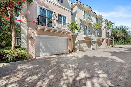 Attached townhomes with balconies and garage doors along a brick-paved drive; red markup points to one balcony.
