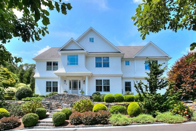 White two-story house with blue shutters, stone front steps, and a landscaped yard.