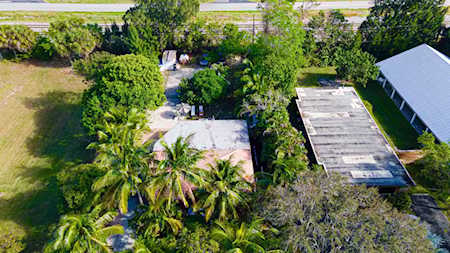 Aerial view of homes surrounded by palms and dense greenery beside a road.