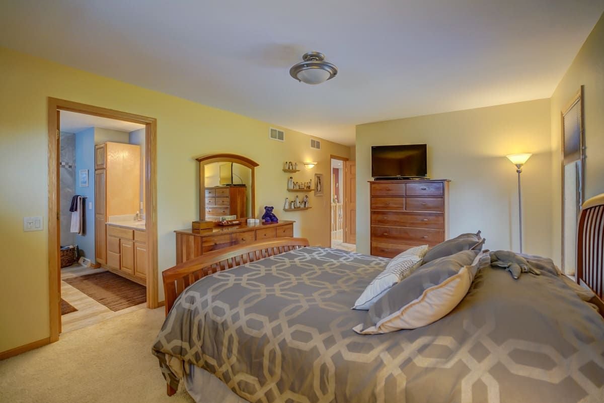 Furnished bedroom with geometric bedding, wooden dressers, and an adjoining bathroom.