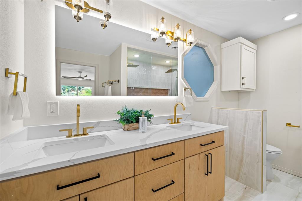 Bathroom with a light wood vanity, marble-look countertop, gold fixtures, and blue octagonal window.