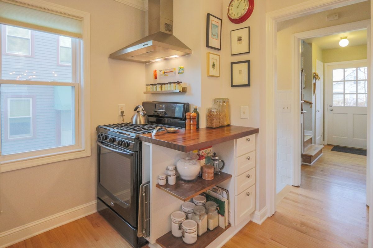 Kitchen with a black gas range, butcher-block counter, and open shelves beside the entry hall.