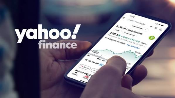 A hand checks stock information on a smartphone beside the Yahoo Finance logo.