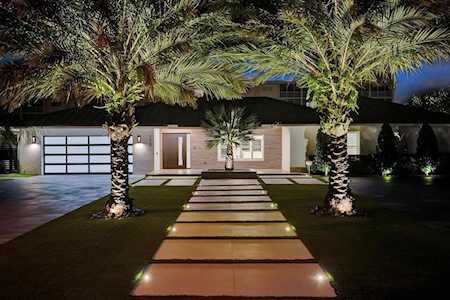 Modern home at night with palm trees and an illuminated walkway to the entry.