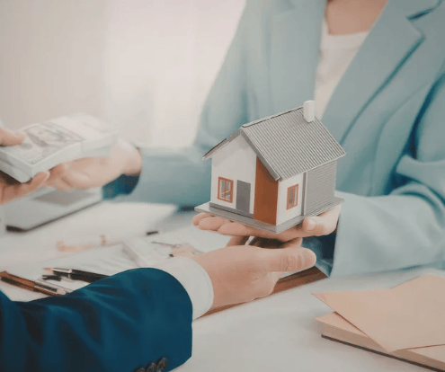 People discuss a home sale, holding a model house and cash over paperwork.