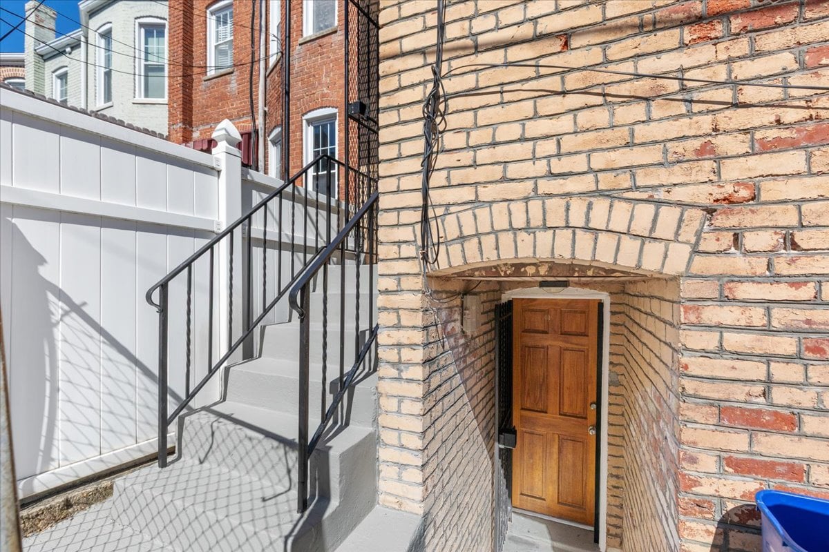 Brick building entrance with an arched recess, wooden door, and white steps with black railings.