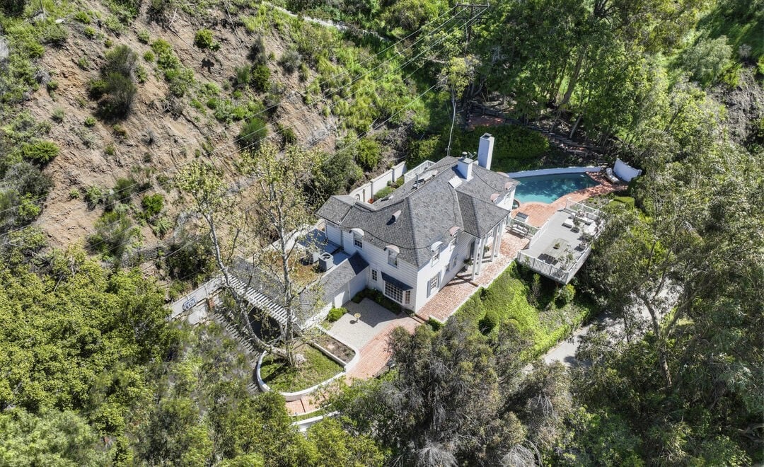 Aerial view of Lindsay Lohan’s former sanctuary on San Ysidro Drive in Beverly Hills, a secluded two-story traditional estate nestled against a canyon hillside, featuring brick pathways, a sun-drenched terrace, and a private swimming pool. This iconic residence, later spotlighted by top Los Angeles real estate agent Brendan Brown, embodies emotional retreat and Hollywood reinvention.